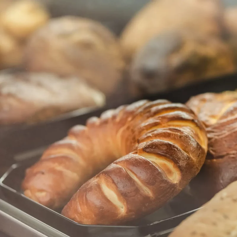 Many different pastries lie behind a glass window of a bakery shop